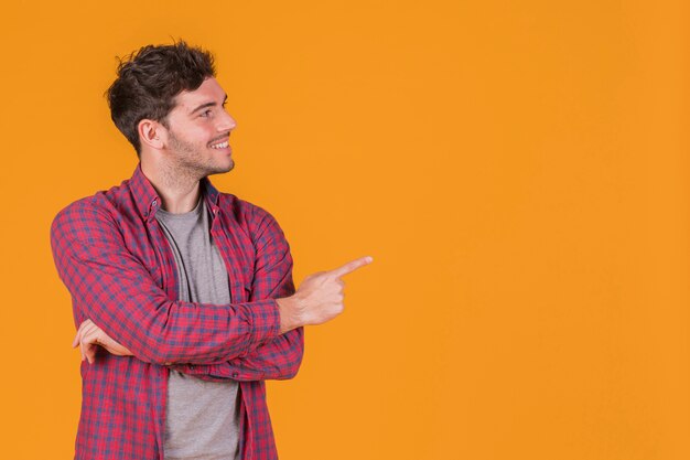 Smiling portrait of a young man pointing his finger against an orange backdrop