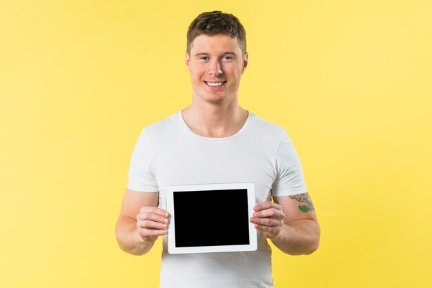Smiling portrait of a young man showing digital tablet against yellow backdrop