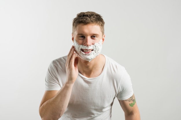 Smiling portrait of a young man touching his cheeks with hand against white backdrop