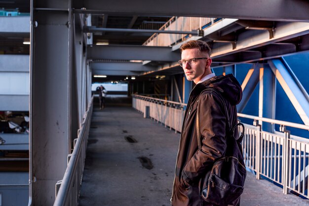 Smiling portrait of young man with backpack on his shoulder standing on the bridge