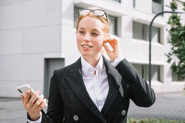 Smiling portrait of a young woman adjusting the bluetooth holding mobile phone in hand