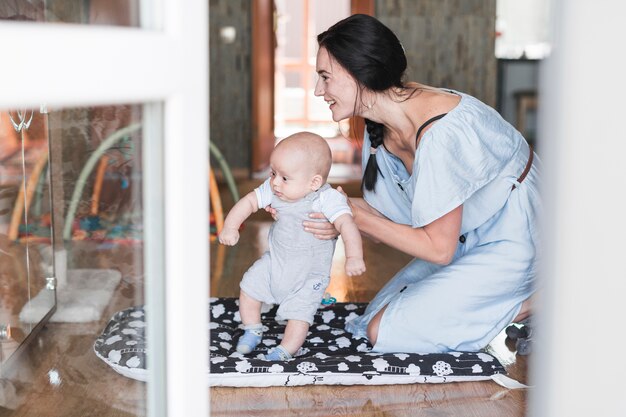 Smiling portrait of young woman playing with her baby at home