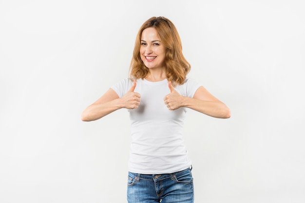 Smiling portrait of a young woman showing thumb up sign against white background