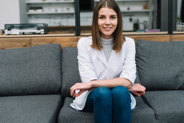 Smiling portrait of a young woman sitting on gray sofa looking at camera