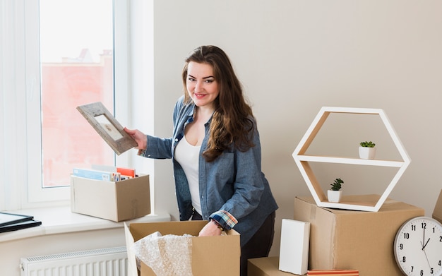 Smiling portrait of a young woman unpacking the cardboard boxes