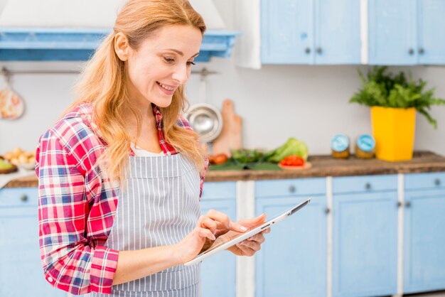 Smiling portrait of a young woman using digital tablet in the kitchen