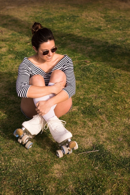 Foto gratuita ritratto sorridente di una giovane donna con le sue gambe attraversate che si siedono sull'erba verde