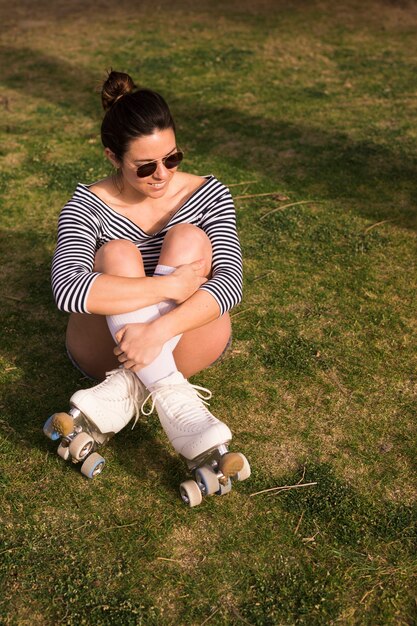 Smiling portrait of a young woman with her crossed legs sitting on green grass