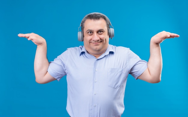 Smiling and positive man in blue shirt wearing headphones pretending that he is flying holding his hands up on a blue background