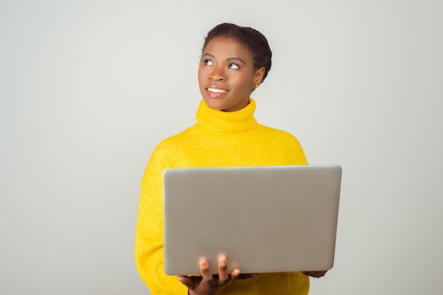 Smiling positive pc user holding laptop and looking away