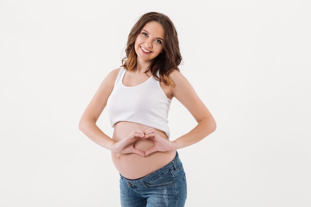 Smiling pregnant woman standing showing heart love gesture.