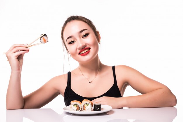 Smiling pretty asian look with modest hairdo sit on the table eat sushi rolls smiling isolated on white