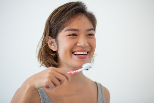 Smiling pretty Asian woman brushing teeth