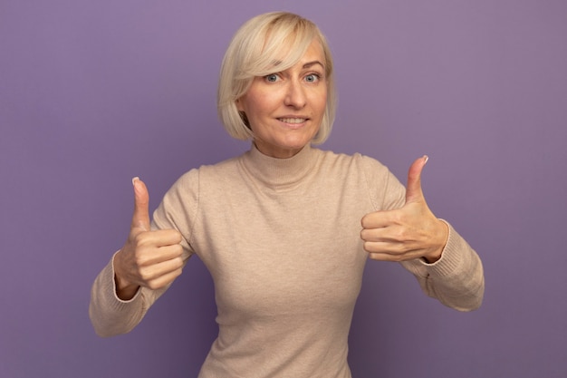 Smiling pretty blonde slavic woman thumbs up of two hands on purple