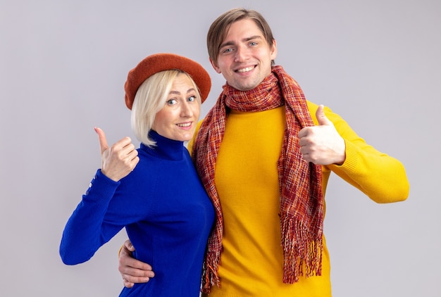 Smiling pretty blonde woman with beret and handsome slavic man with scarf around his neck thumb up isolated on white wall with copy space