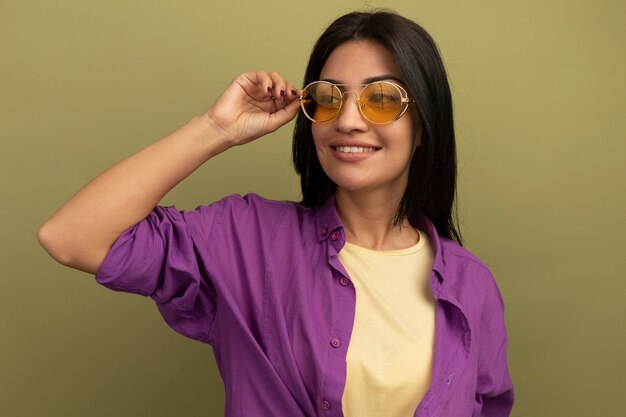 Smiling pretty brunette caucasian girl in sun glasses looks at side on olive green