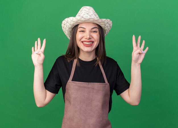 Smiling pretty caucasian female gardener wearing gardening hat gesturing eight with fingers on green