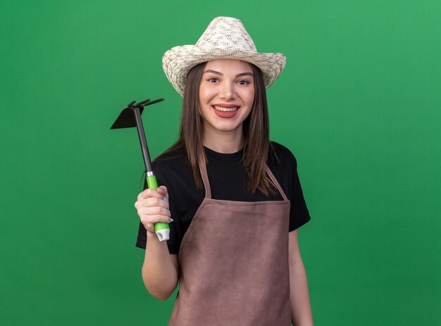 Smiling pretty caucasian female gardener wearing gardening hat holding hoe rake