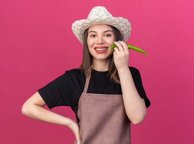 Smiling pretty caucasian female gardener wearing gardening hat holding hot pepper