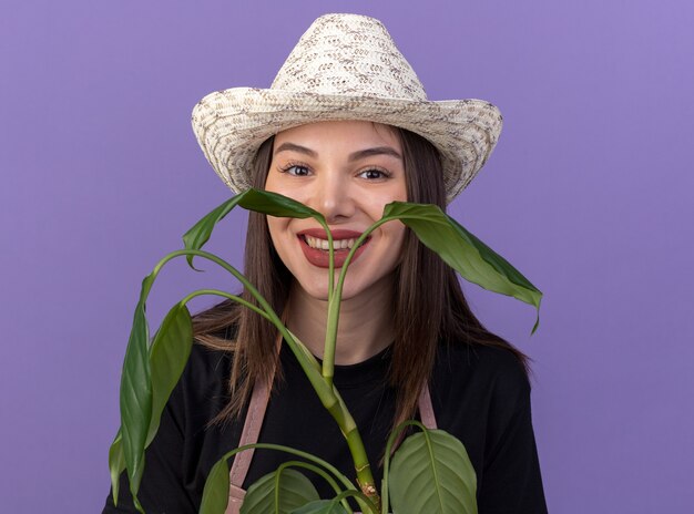 Smiling pretty caucasian female gardener wearing gardening hat holds plant branch