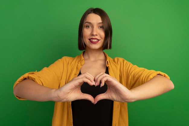 Smiling pretty caucasian woman gestures heart hand sign on green