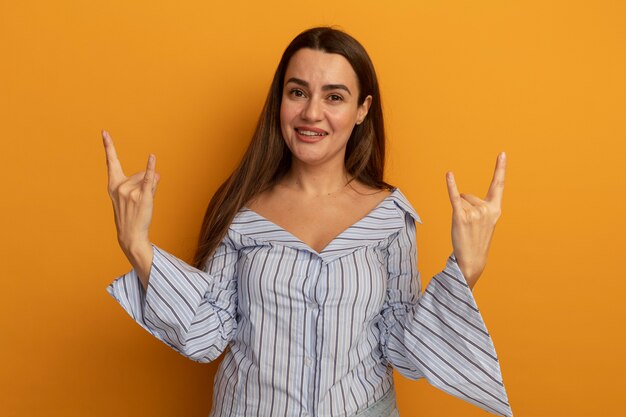 Smiling pretty caucasian woman gestures horns with two hands on orange