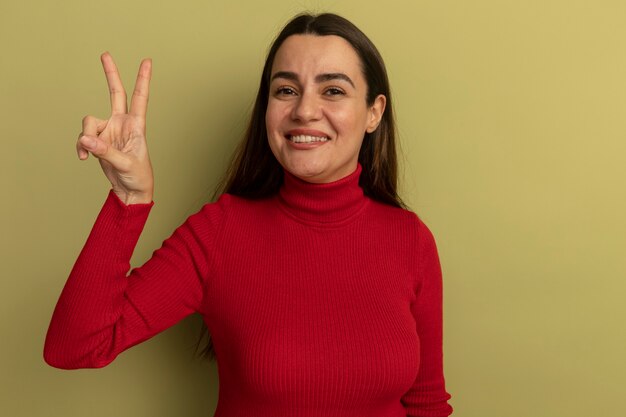 Smiling pretty caucasian woman gestures victory hand sign on olive green