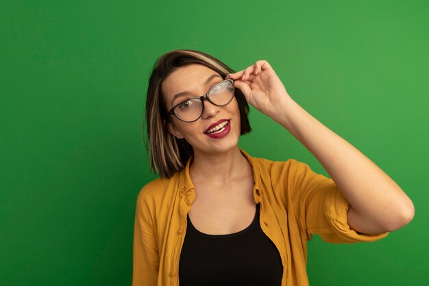 Smiling pretty caucasian woman looking at camera through optical glasses on green