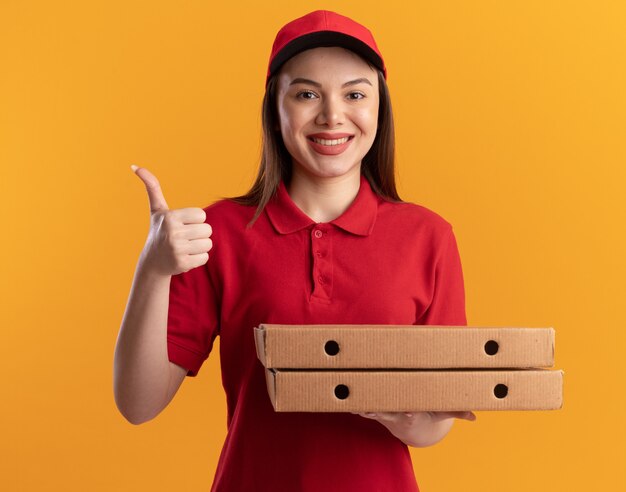 Smiling pretty delivery woman in uniform thumbs up and holds pizza boxes