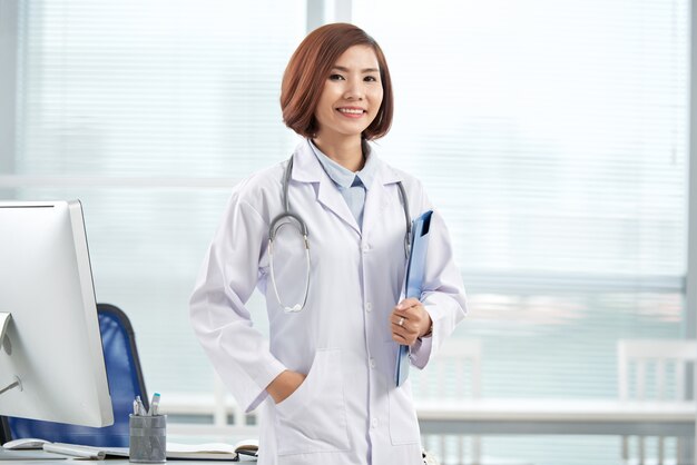 Smiling pretty doctor standing in the hospital office with a paper folder