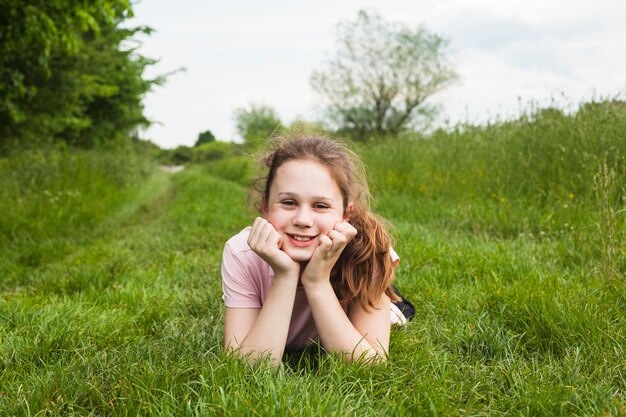 公園で緑の草の上に横たわる笑顔のかわいい女の子