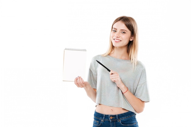 Smiling pretty girl pointing pen on a blank paper notebook