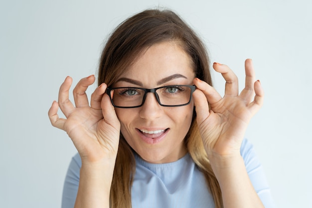 Smiling pretty woman adjusting glasses and looking at camera.