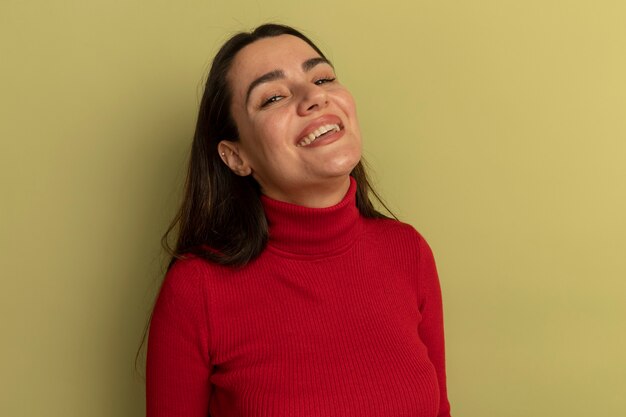 Donna graziosa sorridente che esamina fronte isolato sulla parete verde oliva