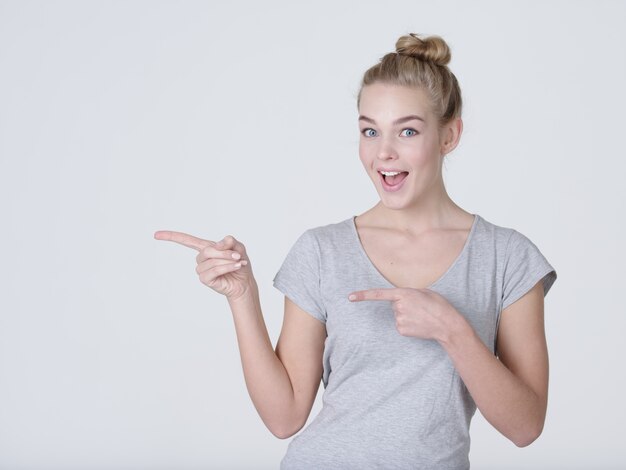 Smiling pretty woman pointing finger away over gray background. Looking at camera
