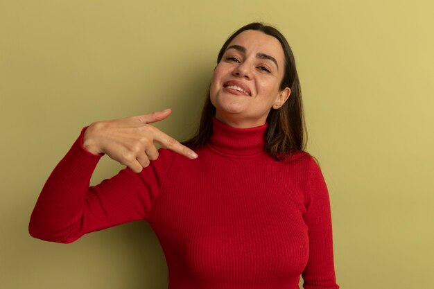 Smiling pretty woman points at side isolated on olive green wall