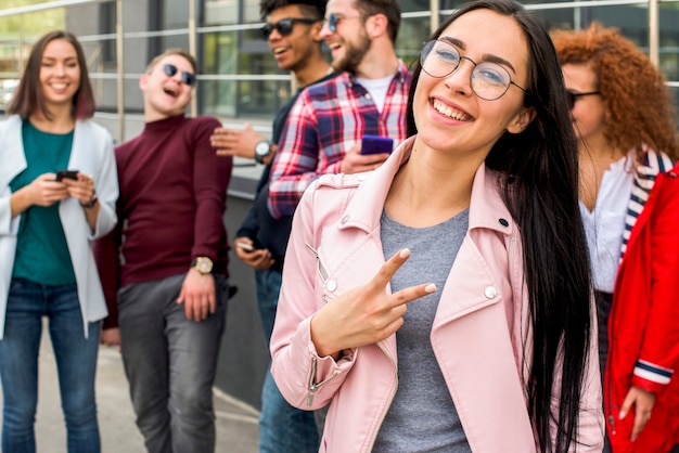 Smiling pretty woman standing in front of her friends gesturing victory sign