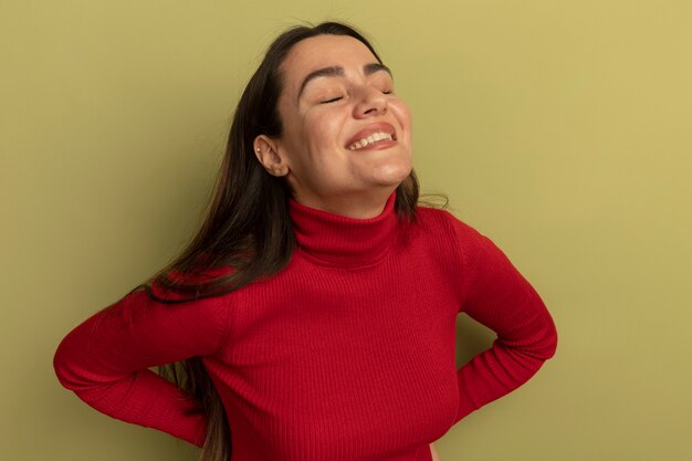 Smiling pretty woman stands with closed eyes isolated on olive green wall