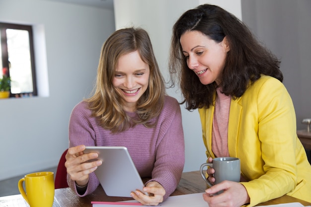 Smiling pretty women drinking tea and using tablet