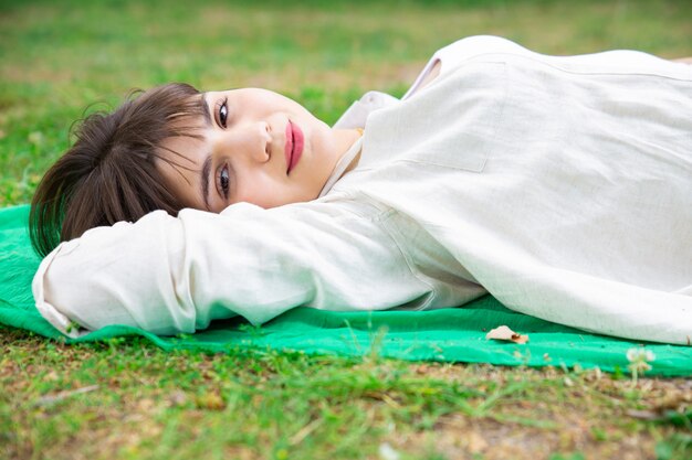 Усмехаясь милая молодая женщина лежа и ослабляя на лужайке