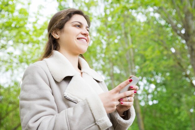 公園でスマートフォンを使用して笑顔のかなり若い女性