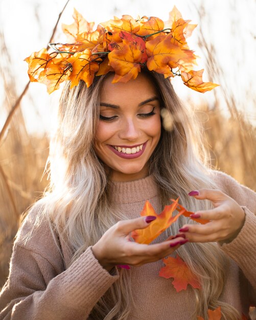 Smiling pretty young woman wearing maple leaves tiara playing with autumn leaves