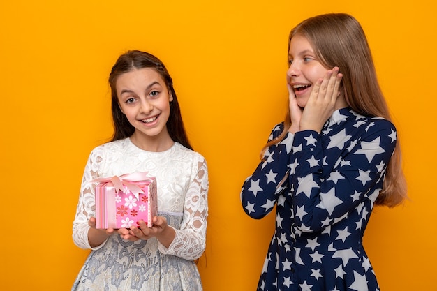 Smiling putting hands on cheeks two little girls holding present