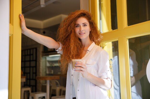 Smiling red hair woman standing and holding cup of coffee