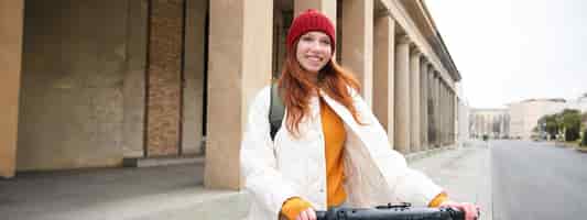 無料写真 笑顔の赤毛のヨーロッパの女の子が公共エスクーターを運転し、観光客が市内中心部の乗り物を探索する