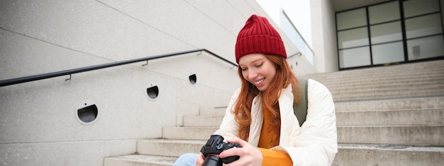 smiling-redhead-girl-photographer-checks-her-shots-holds-camera-looks-screen-takes-photos_1258-196288.jpg