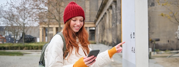 無料写真 笑顔の赤毛の女の子の観光客が街を歩き回り、観光を開催する人気のランドマークを探索する