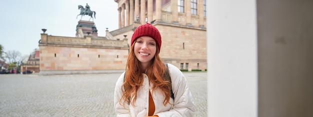 無料写真 笑顔の赤毛の女の子の観光客が街を歩き回り、観光を開催する人気のランドマークを探索する