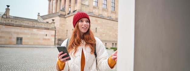 Smiling redhead girl tourist walks around city and explores popular landmarks sightseeing holding