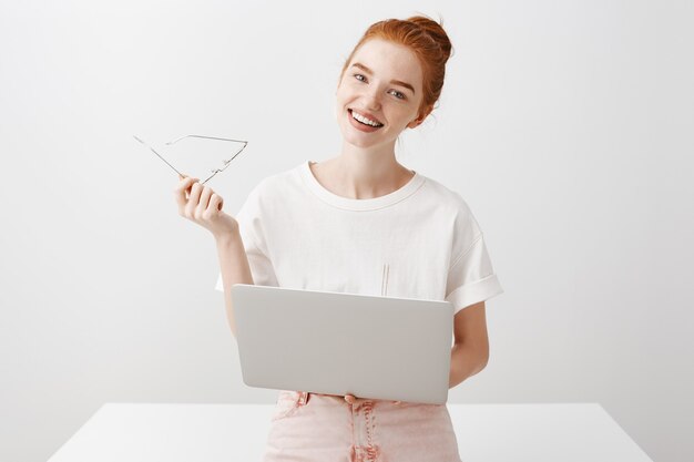 Smiling redhead girl using laptop and looking